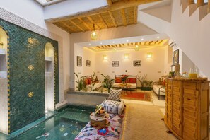 A spacious room with a pool, a wooden cabinet, and a sofa with cushions. - Riad Mama (Marrakech)