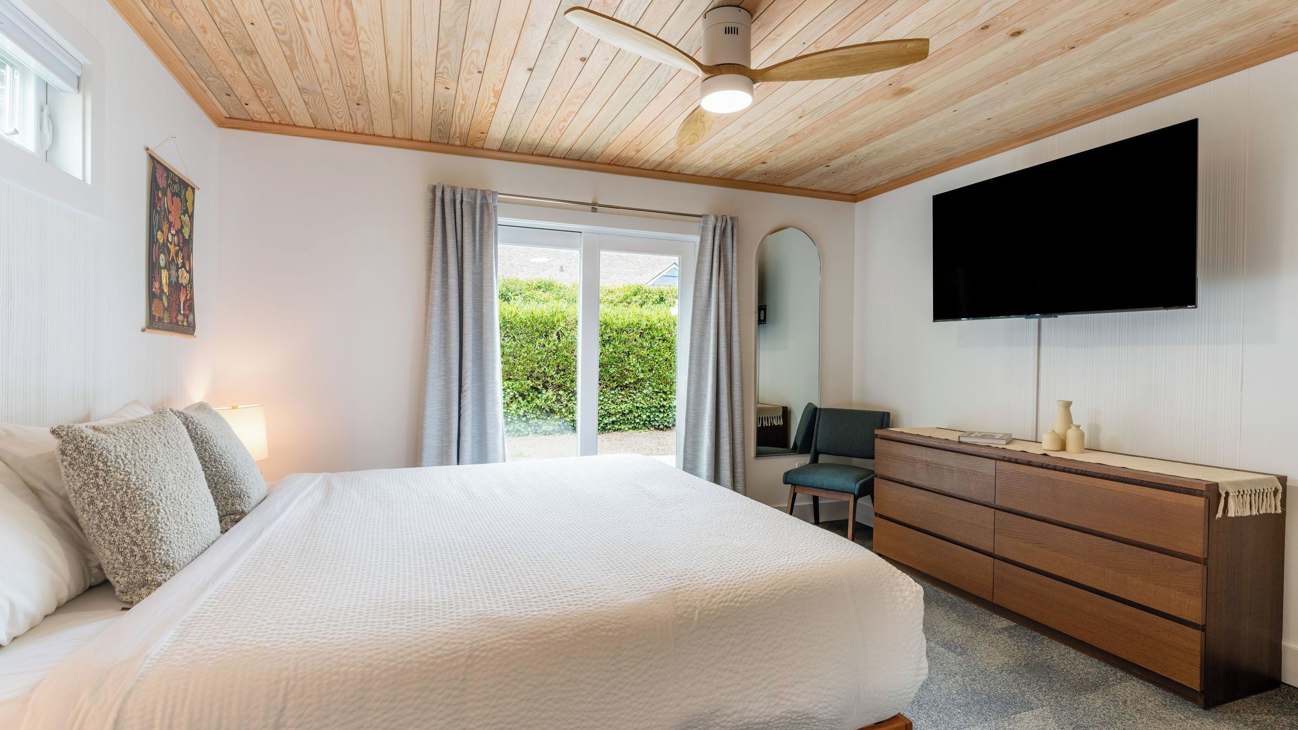 A bedroom with a bed, a dresser, a television, and a window with curtains.