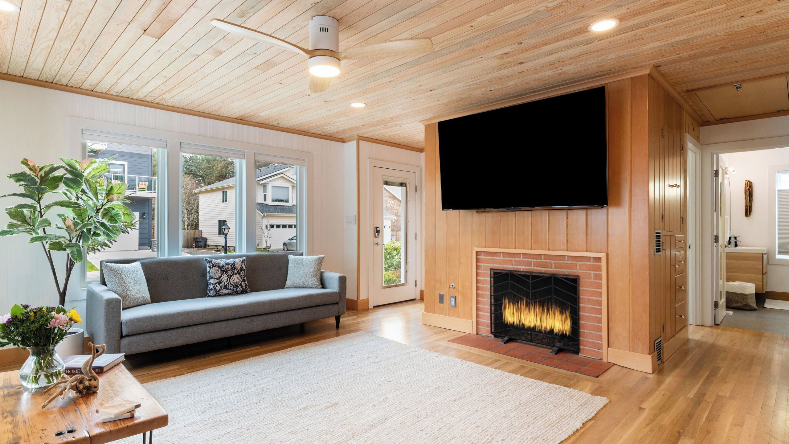 Una sala de estar con chimenea, un sofá, un televisor montado en la pared y vistas al exterior.
