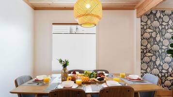 A dining area with a wooden table set for breakfast, a hanging light fixture, and a patterned wallpaper.