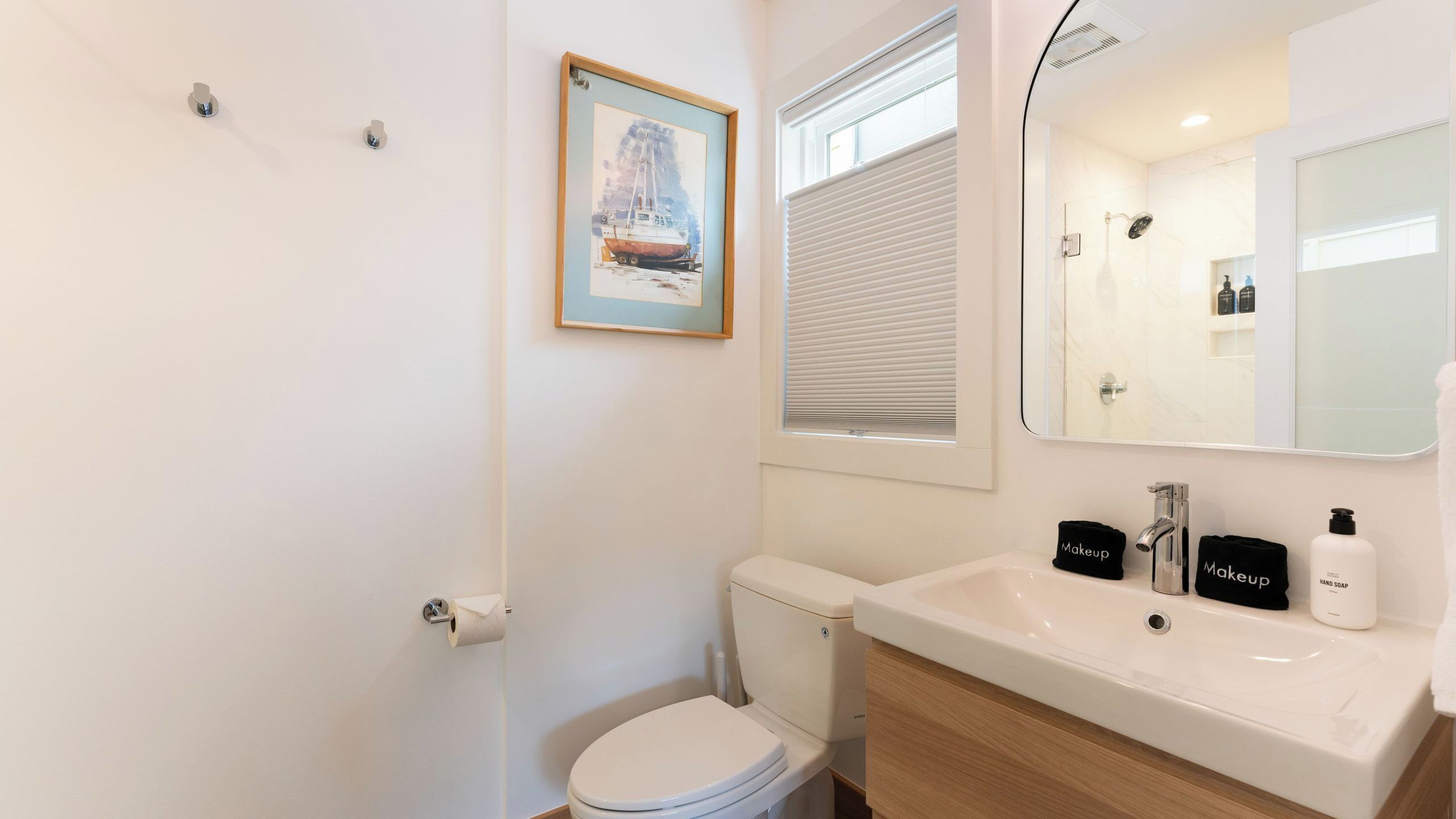 Ein Badezimmer mit Toilette, Waschbecken und Spiegel, inklusive Toilettenartikeln und einem gerahmten Bild an der Wand.
