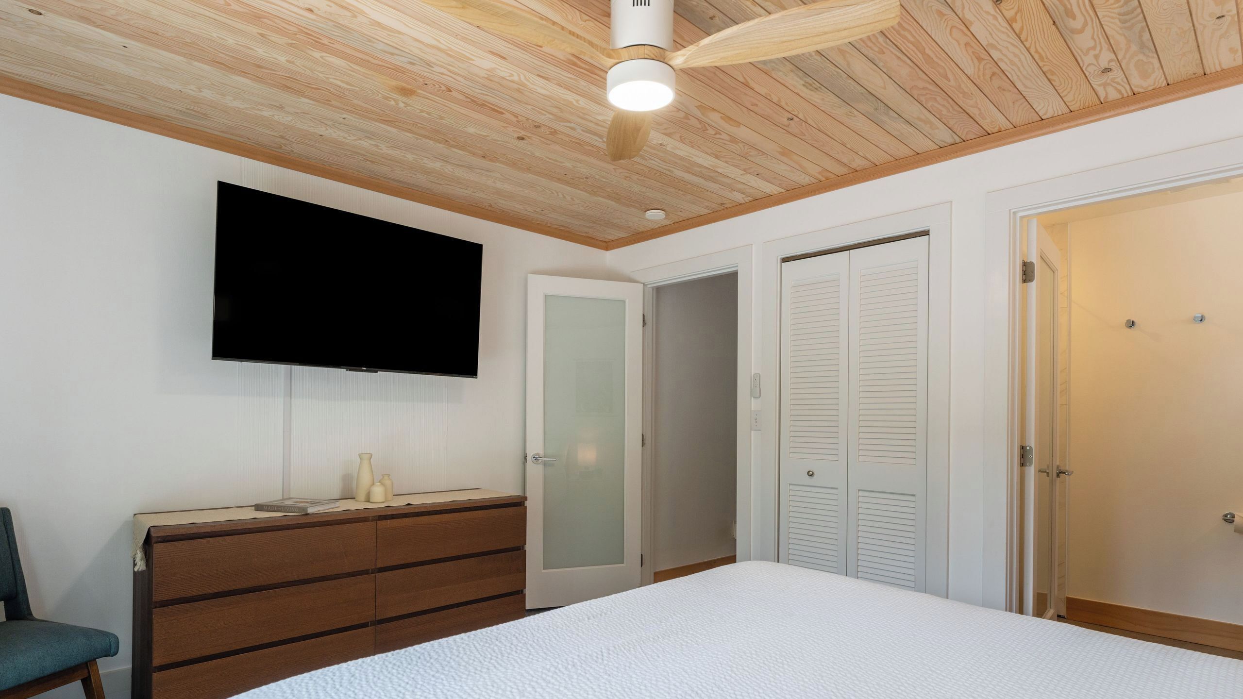 A bedroom with a bed, a dresser, a television, a ceiling fan, and a closet.
