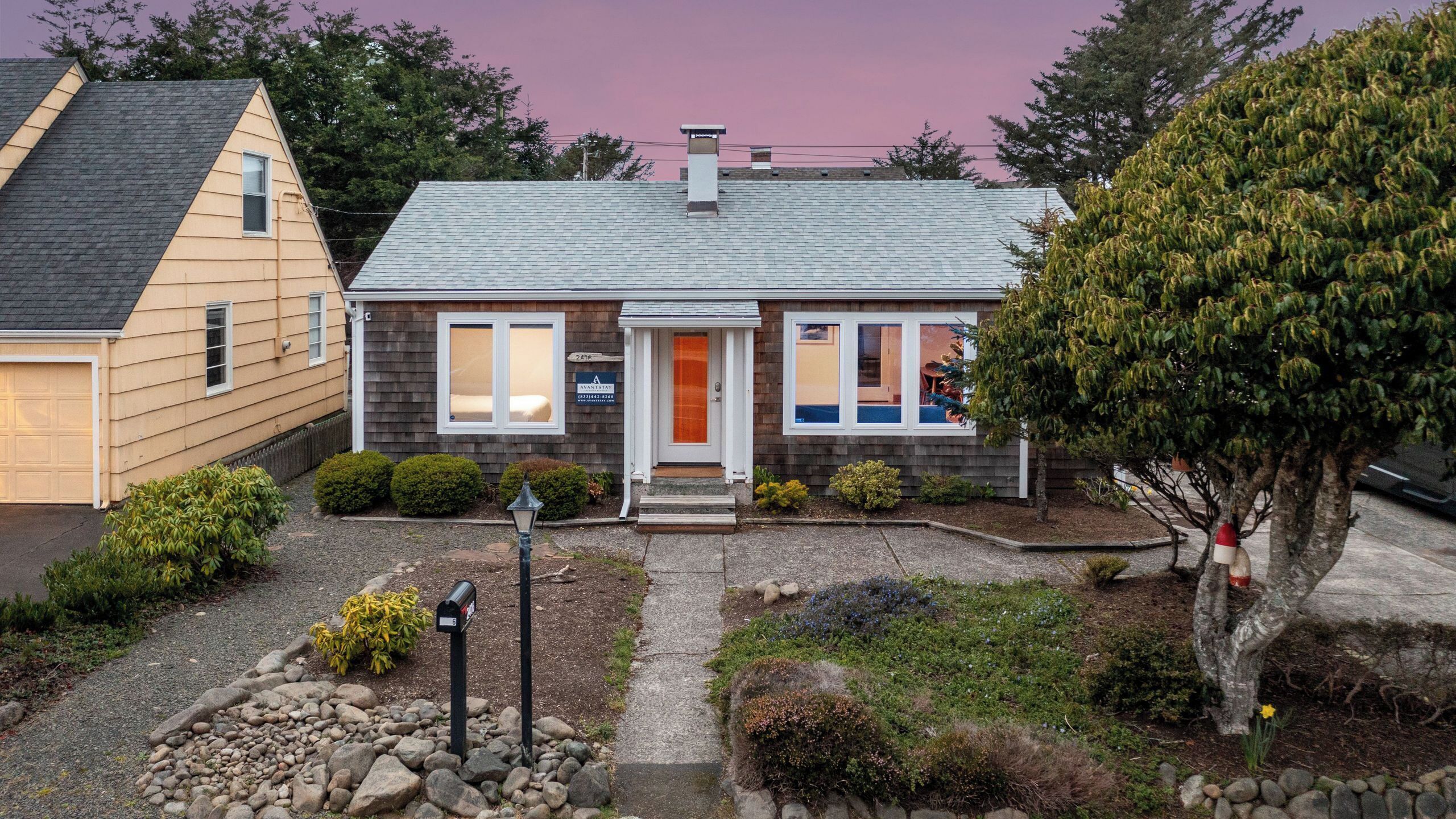 A two-story house with a front porch, a garage, and a well-maintained garden with rocks and shrubs.