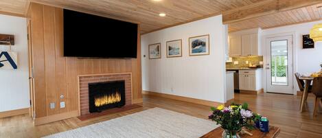 Een moderne woonkamer met een open haard, houten plafond en een flatscreen televisie erboven.