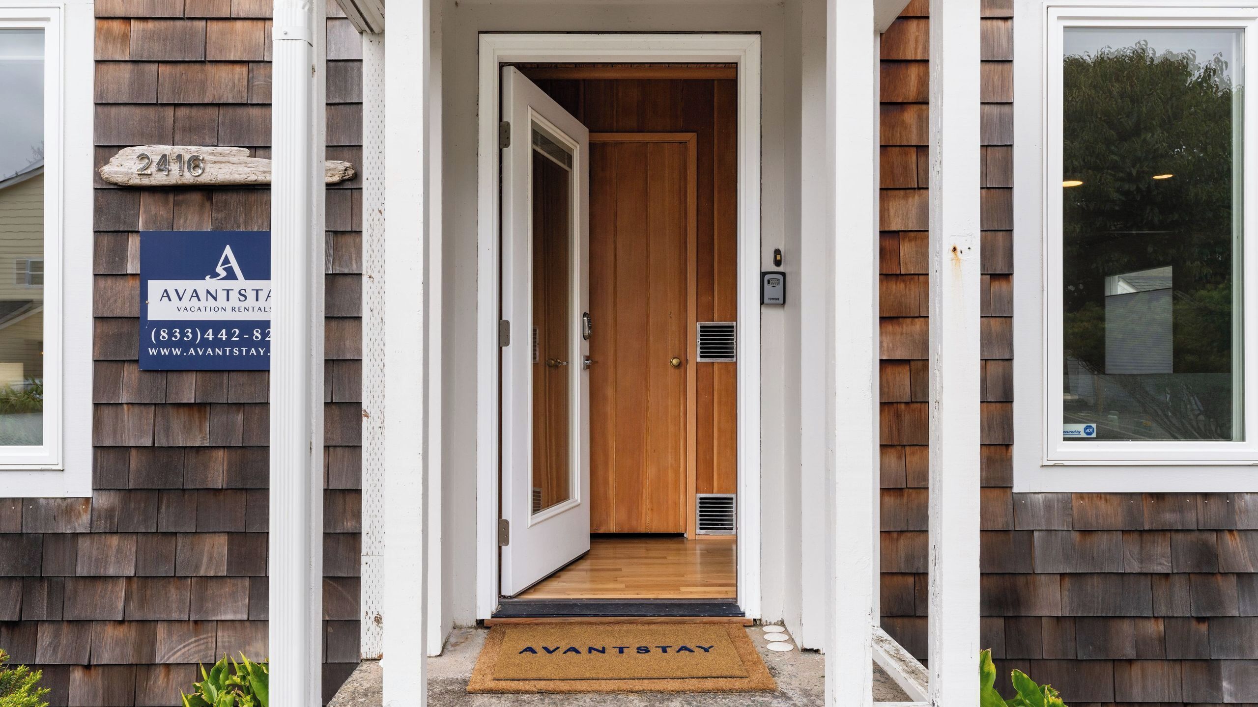 Entrada de una casa de madera con puerta, buzón y felpudo.