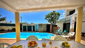 Ein Frühstückstisch am Pool mit Stühlen und Blick auf Pool sowie Gebäude im Hintergrund.