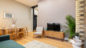 A modern living room with a wooden dining table, a sofa, a TV, and a bookshelf. - Prime Covent Garden gem with Air-Con (London)