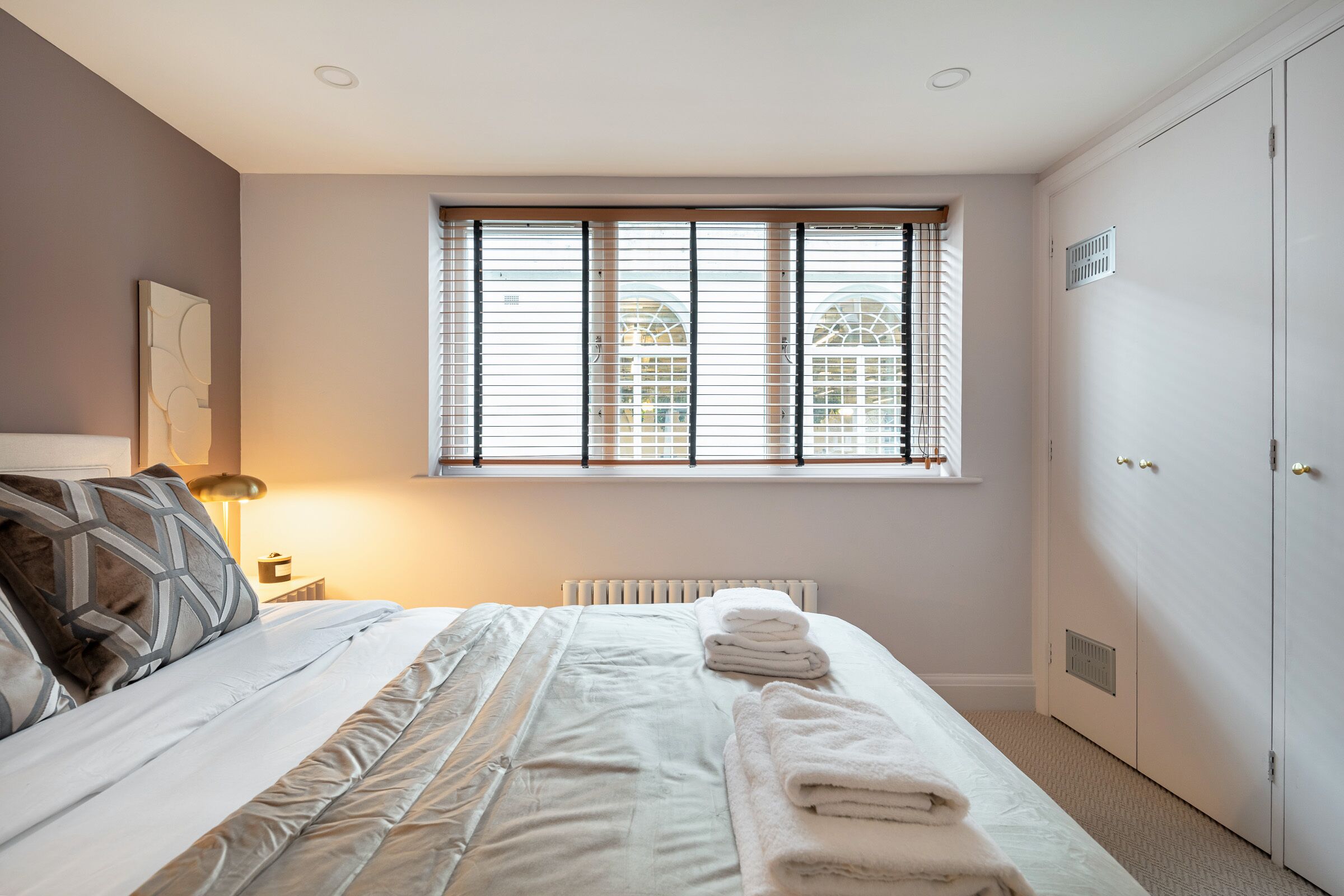 Une chambre à coucher avec un lit, un radiateur, une fenêtre avec des stores et une armoire.