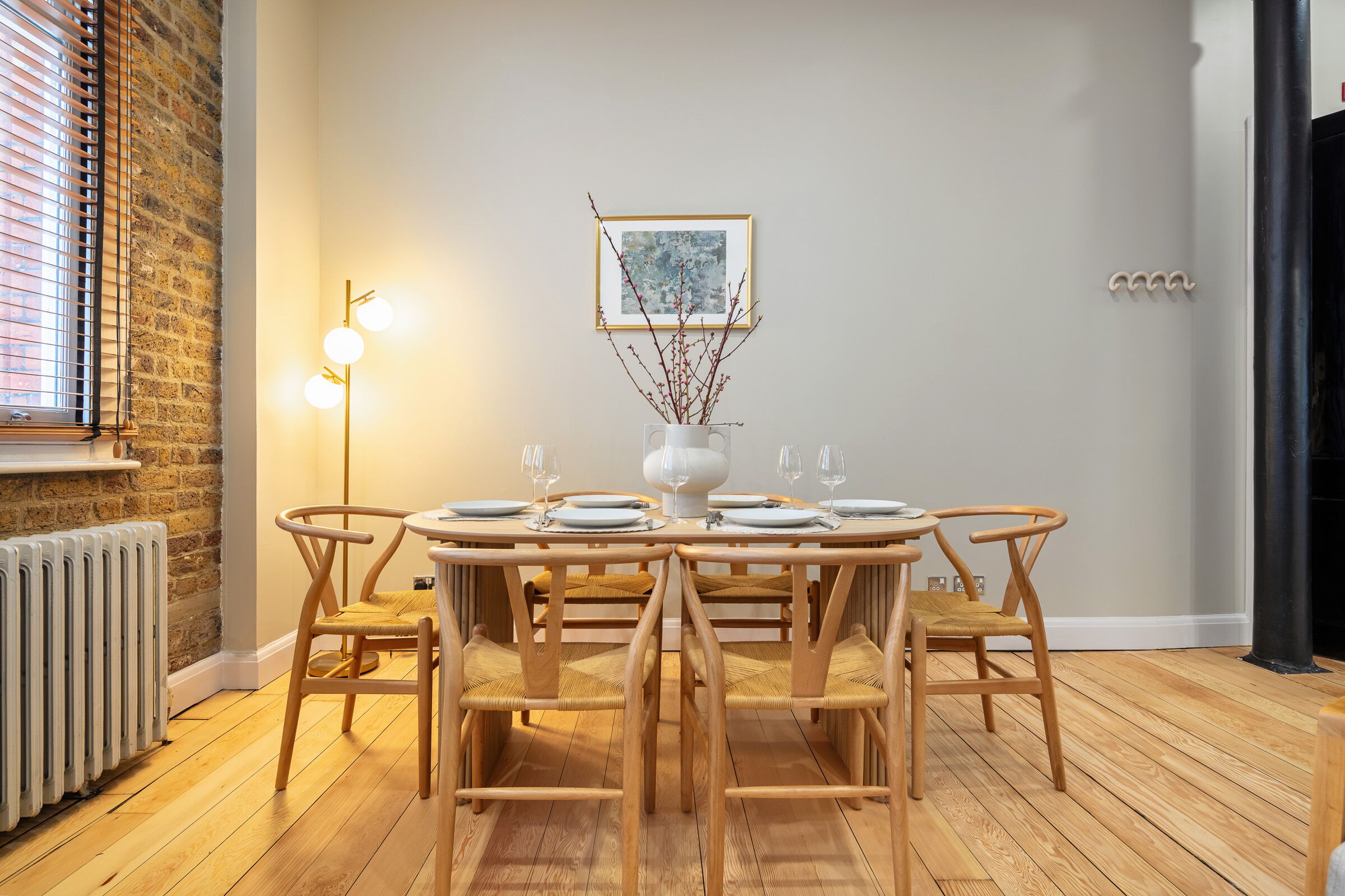 A dining area with a round wooden table set for four, surrounded by four matching chairs. A white vase with branches is placed on the table.