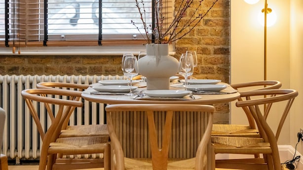 A dining area with a round table set for four, surrounded by wooden chairs. A vase with branches is on the table, and a floor lamp is to the right. - Prime Covent Garden gem with Air-Con (London)