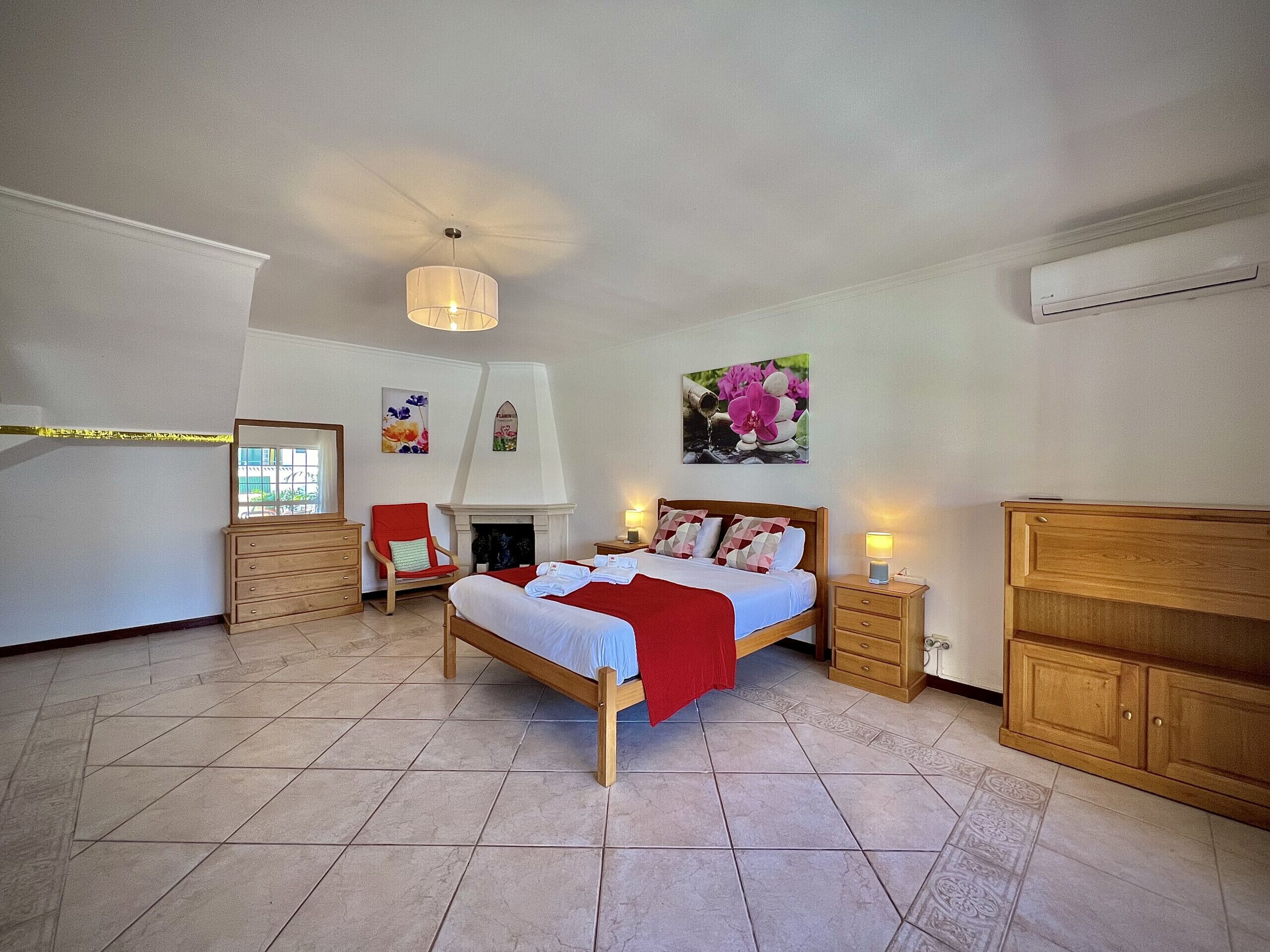 Une chambre à coucher avec un lit, une chaise, une commode, une cheminée et un tableau au mur.