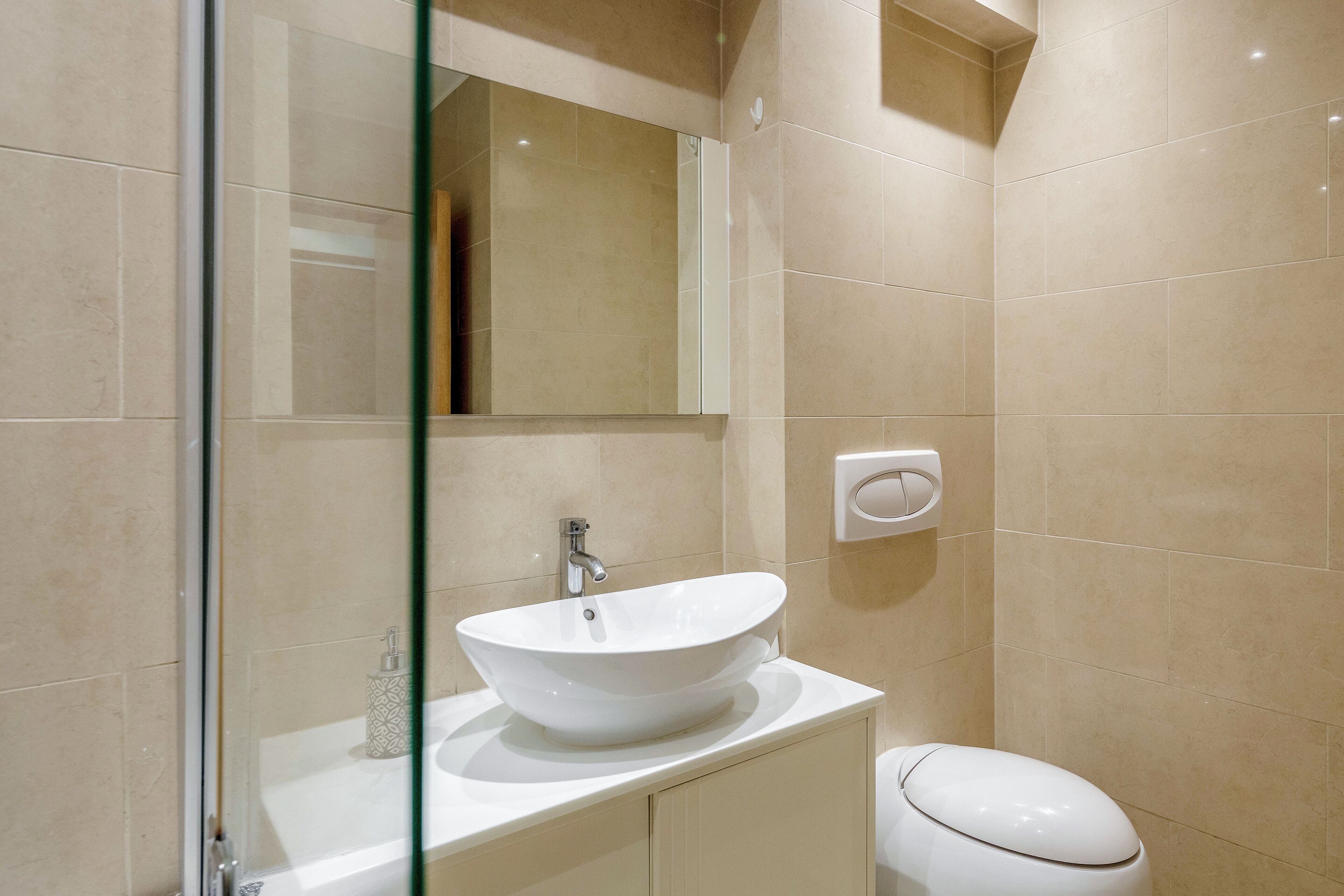 A modern bathroom with a glass shower enclosure, a white sink with a vessel basin, and a toilet.