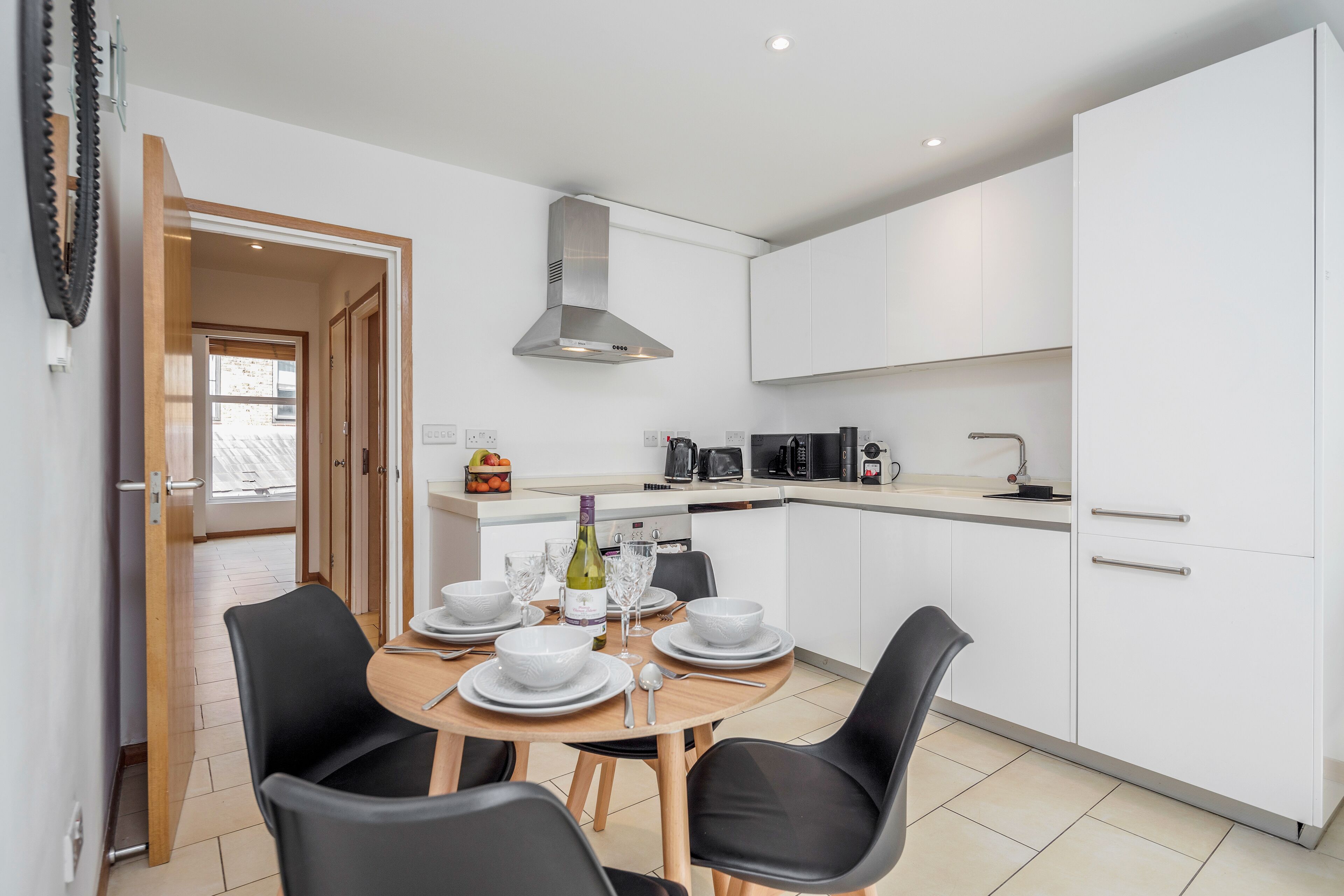 A modern kitchen with white cabinets, a stainless steel range hood, and a dining area with a round table set for four.
