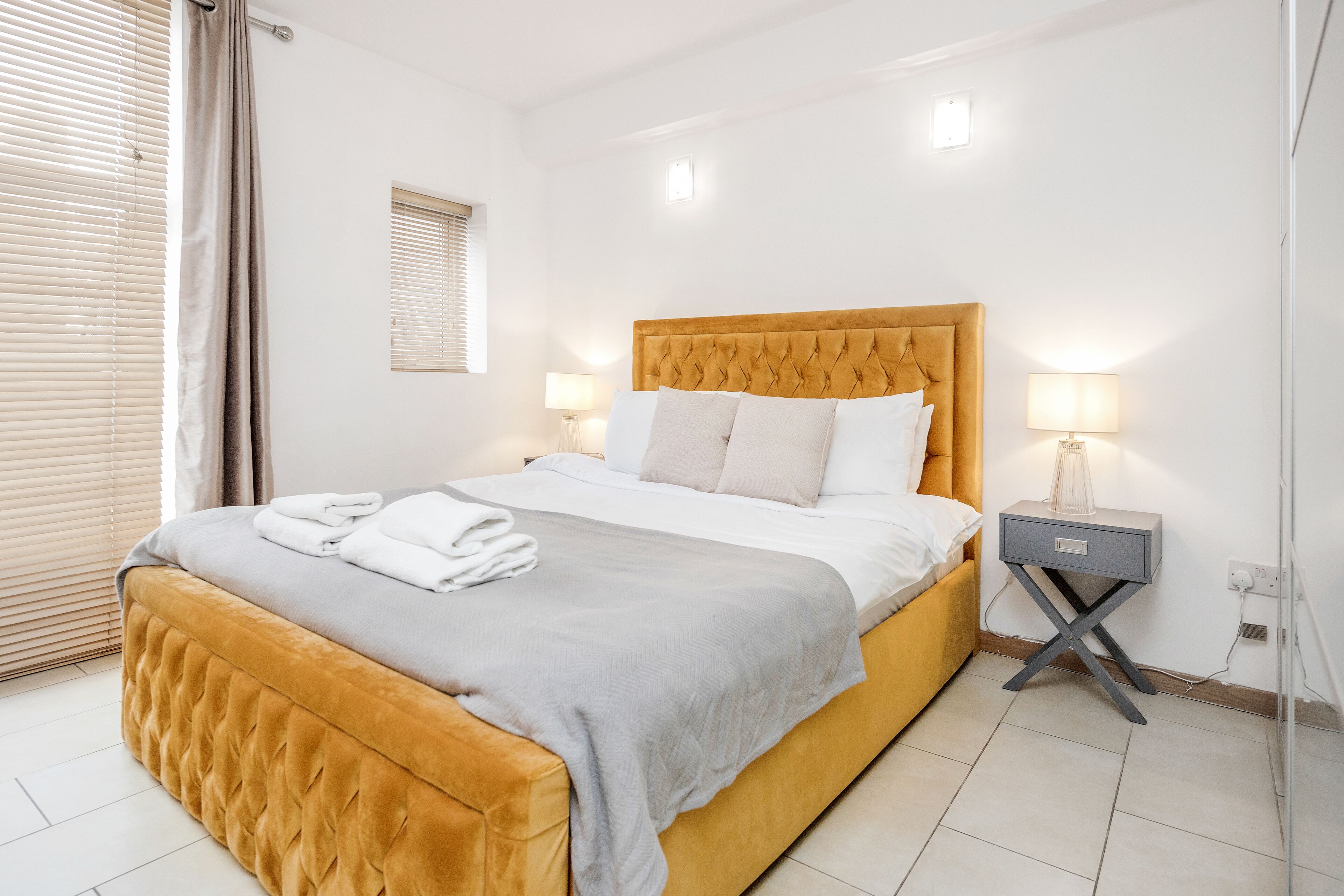 A neatly made bed with a headboard, two bedside lamps, and a bedside table with a lamp.