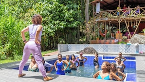 Un groupe de personnes se trouve dans un espace autour d’une piscine, avec une terrasse en bois et un coin salon abrité.
