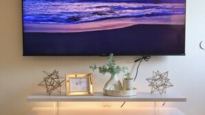 Un salon moderne avec un téléviseur à écran plat fixé au mur, une console blanche agrémentée d’objets décoratifs et une plante en pot placée au premier plan.