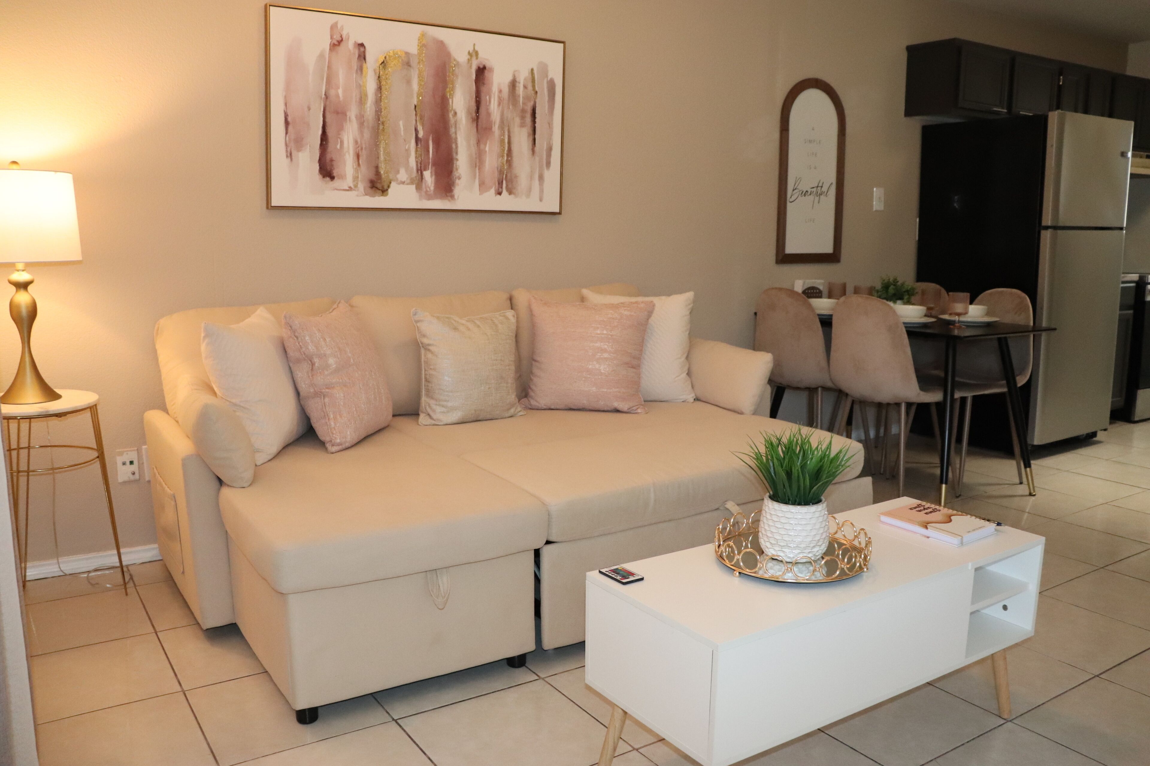 Een moderne woonkamer met een beige bank, een witte salontafel en een keuken op de achtergrond.