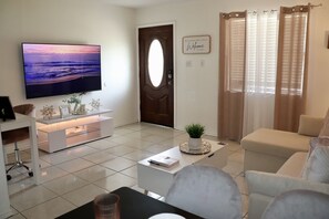 A modern living room with a flat-screen TV, a sofa, a coffee table, and a door with a sign. - Frontier Traveler Stay  (Eagle Pass)