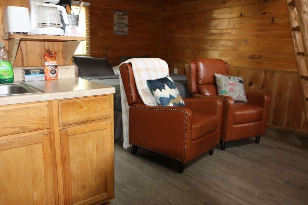Un interior de cabaña acogedor con detalles de madera, una kitchenette y dos sillones de cuero con cojines.