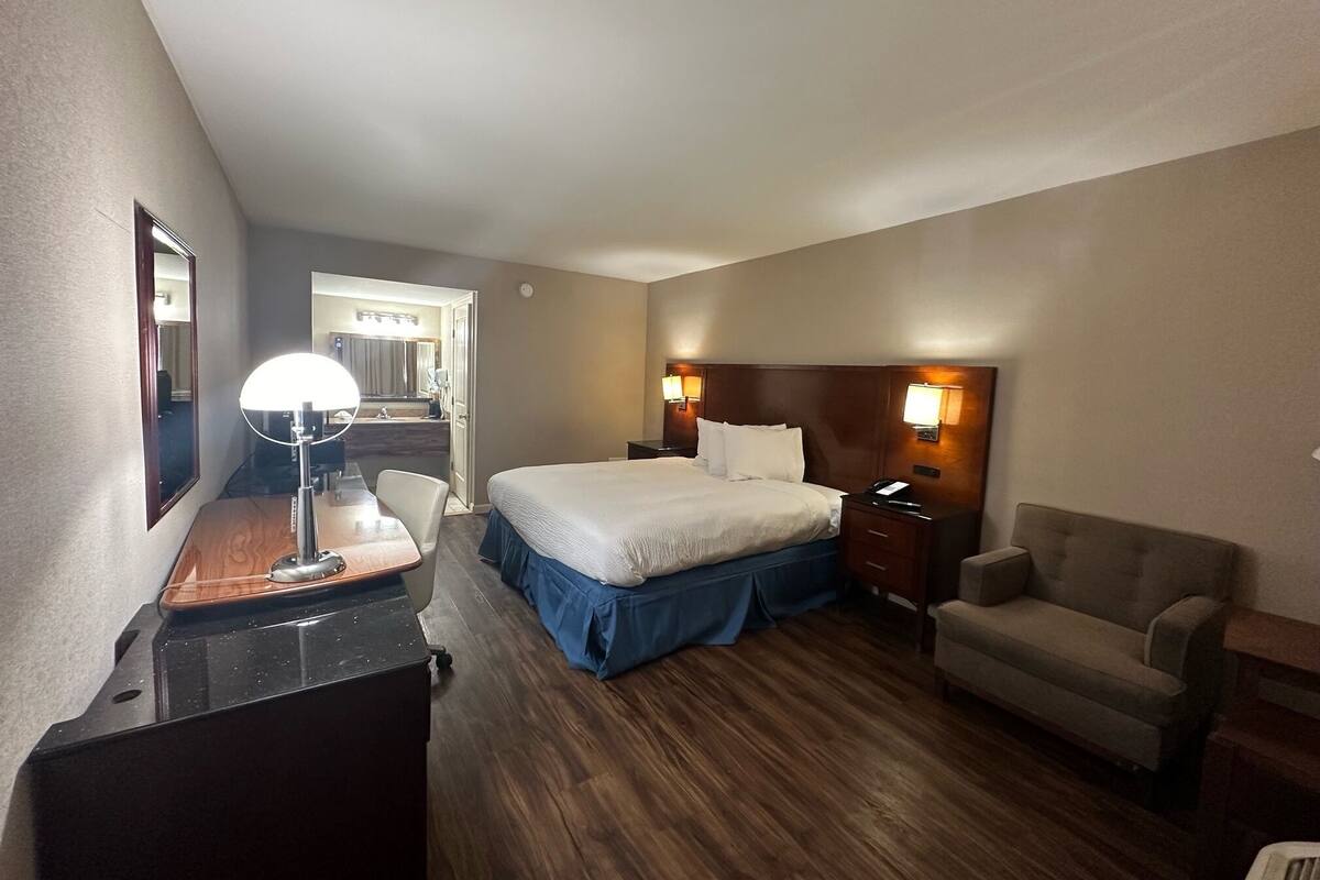 Ett hotellrum med en säng, ett skrivbord med en lampa, en stol och ett nattduksbord med en telefon.