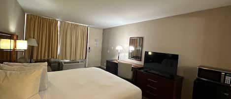 A hotel room with a large bed, a desk with a flat-screen TV, a microwave, and a dresser.