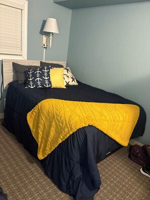 Un lit avec une couverture bleu marine et jaune, une lampe et un mur à la finition texturée.