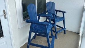 Kaksi sinistä Adirondack-tuolia ja pieni pöytä betoniterassilla, valkoisen oven vieressä.