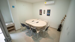 Une salle de conférence avec une table ronde, quatre chaises, un petit bureau avec une chaise et une étagère. Trois tableaux encadrés sont accrochés au mur.