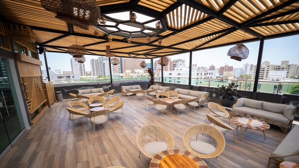 Un vaste salon sur le toit, doté d’un plancher en bois, de meubles en osier et de grandes fenêtres offrant une vue sur la ville.
