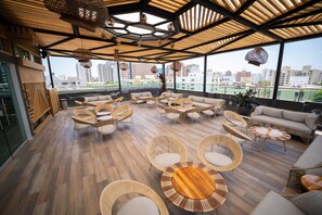 Spaziosa terrazza lounge con pavimento in legno, mobili in vimini e ampie finestre che offrono vista sulla città.