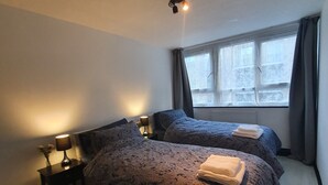 A bedroom with two beds, a window with curtains, a ceiling light, and a nightstand with a lamp. - 3Beds Family Friendly in London with good transport links. Close to Victoria (London)