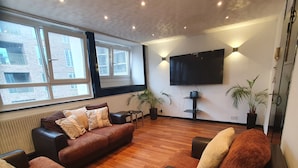 A modern living room with leather sofas, a flat-screen TV mounted on the wall, and large windows offering a view of the cityscape. - 3Beds Family Friendly in London with good transport links. Close to Victoria (London)