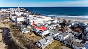 An aerial view of a coastal residential area with houses, a beach, and a road.