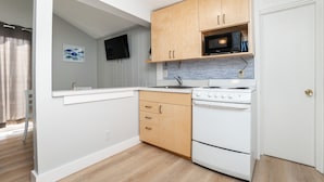 A compact kitchen with wooden cabinets, a microwave, a stove, and a tiled backsplash.