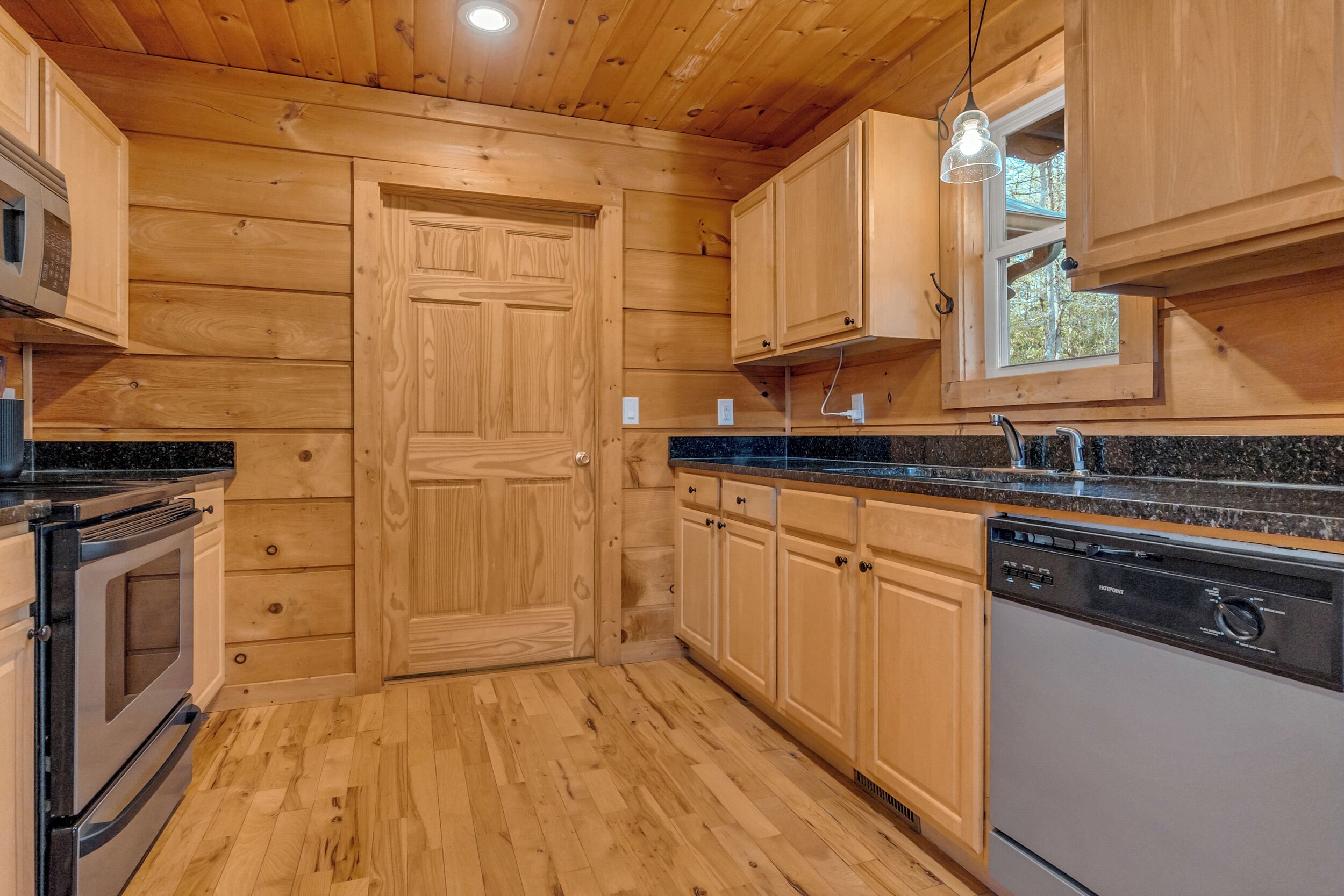 Una cocina con paneles de madera, horno empotrado, microondas y lavavajillas.