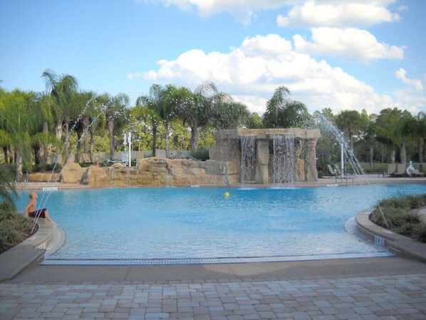 A swimming pool with a waterfall feature, surrounded by palm trees and a paved walkway. - !!Getaway 20 % Deal!!Beautiful Townhome with Private Pool near Disney (Kissimmee)