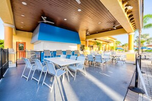 An outdoor patio area with tables and chairs, a large blue and white grill, and a wooden ceiling. - !!Getaway 20 % Deal!!Beautiful Townhome with Private Pool near Disney (Kissimmee)