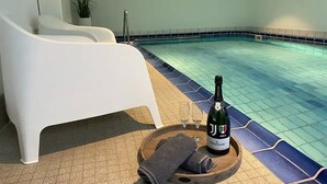 Un área junto a la piscina con una silla de descanso, una botella de vino, copas y una toalla sobre una bandeja de madera.