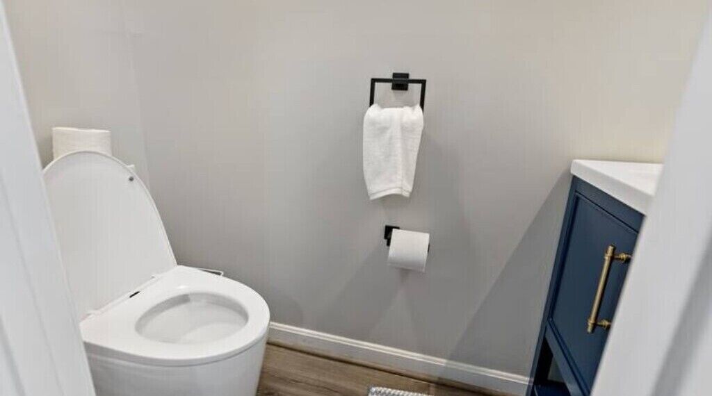 A small bathroom with a white toilet, a blue cabinet, and a towel hanging on a hook.