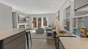 Une cuisine moderne dotée d’un îlot central, un coin repas avec une table et des chaises, et un salon avec un canapé et un téléviseur.