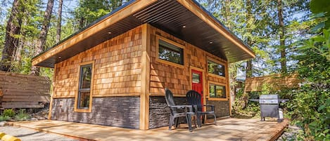 Een houten vakantiehuis met een terras, twee stoelen en een barbecue.