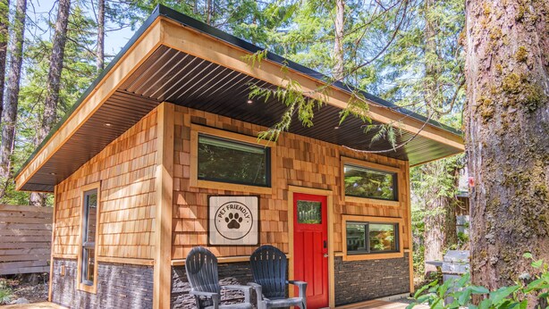 Cabaña que admite mascotas con puerta roja, fachada de madera y dos sillas afuera.