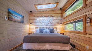 Un dormitorio con una cama grande, paredes de madera, un tragaluz y un cuadro.