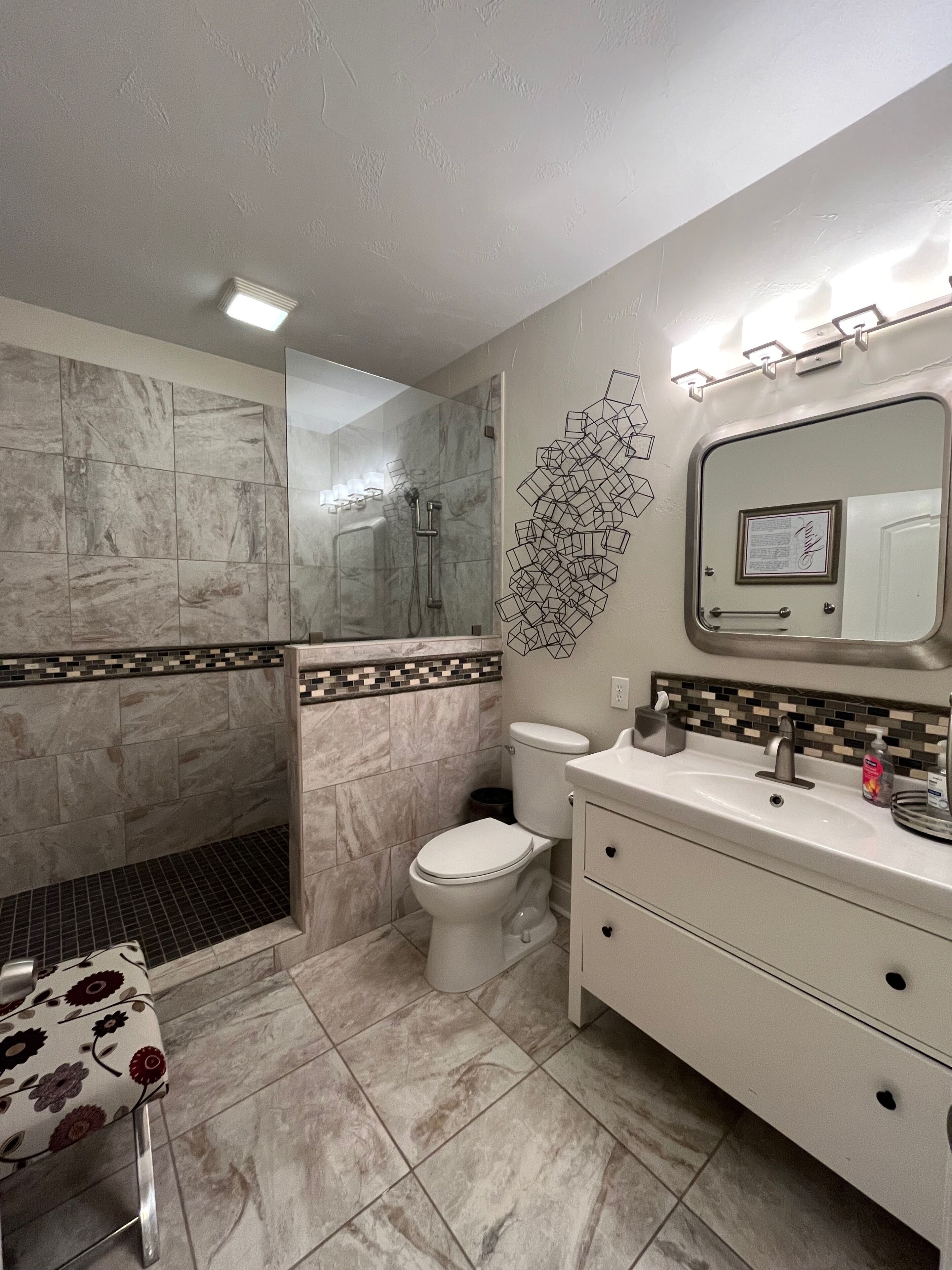 Un baño con ducha, inodoro, lavabo y espejo con iluminación.