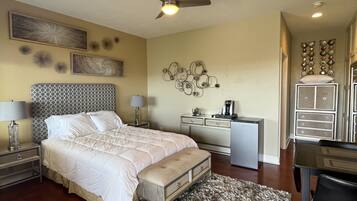 Um quarto com cama, mesas de cabeceira, escrivaninha e ventilador de teto.