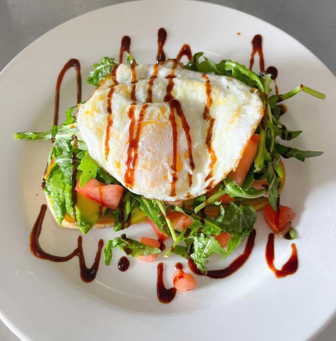 Un plato con un huevo escalfado sobre una ensalada, rociado con salsa.