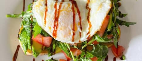 A plate with a poached egg on top of a salad, drizzled with sauce.