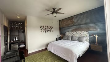 A modern bedroom with a bed, a ceiling fan, a wall art piece, and a nightstand with a lamp.