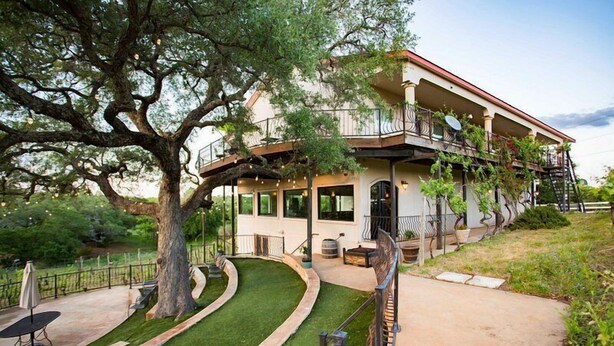 Une maison à deux étages avec un balcon, un arbre dans le jardin et une terrasse dallée.