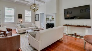 Een ruime woonkamer met een open haard, witte banken, een houten salontafel en een grote tv aan de muur.